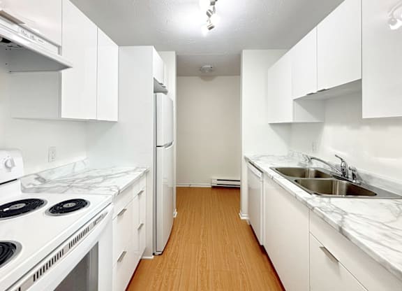 A white kitchen with a stove, refrigerator, and sink.