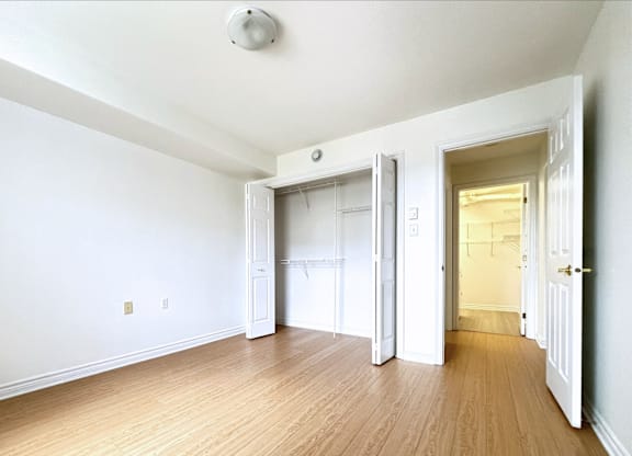 A room with white walls and wooden flooring with a door open to another room.