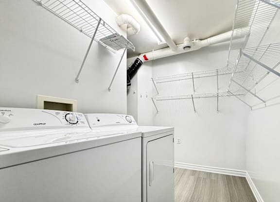 A white washing machine in a laundry room with a fan and shelving above it.