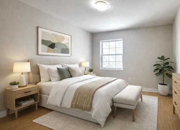 A bedroom with a large bed, a nightstand with a lamp, a window, and a potted plant.