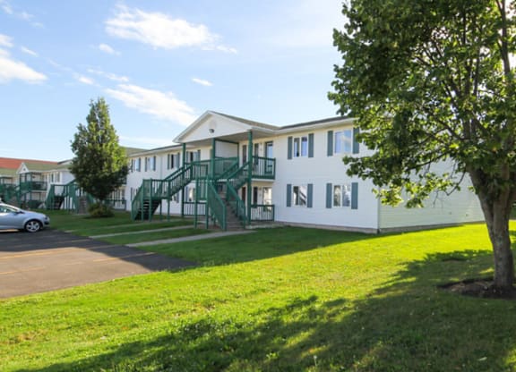 A white building with green railings and a tree in front.