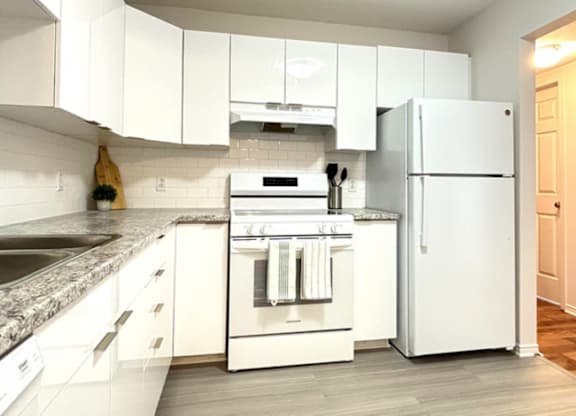 A white kitchen with a refrigerator, oven, and sink.