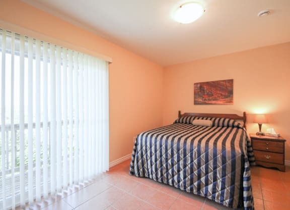 A bedroom with a bed, nightstand, and window with blinds.