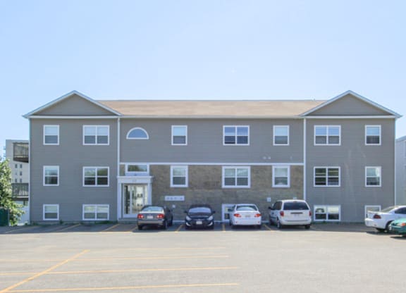 A grey building with a parking lot in front of it.