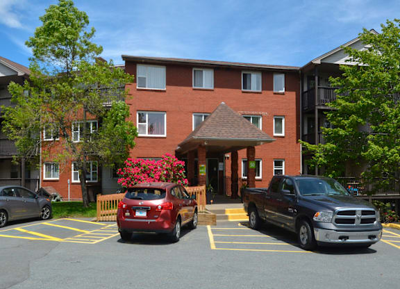 A red car is parked in a parking lot in front of a brick building.