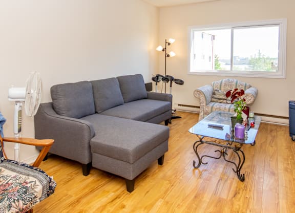 A grey couch sits in a living room with a fan and a chair.