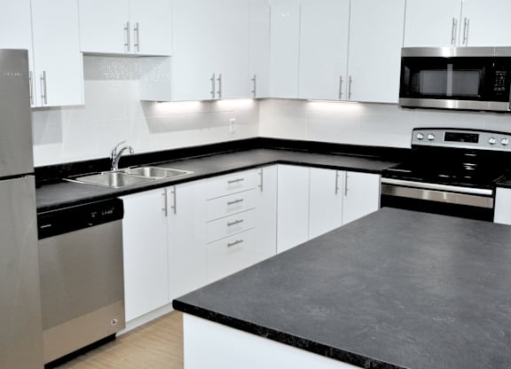 A modern kitchen with white cabinets and black countertops.