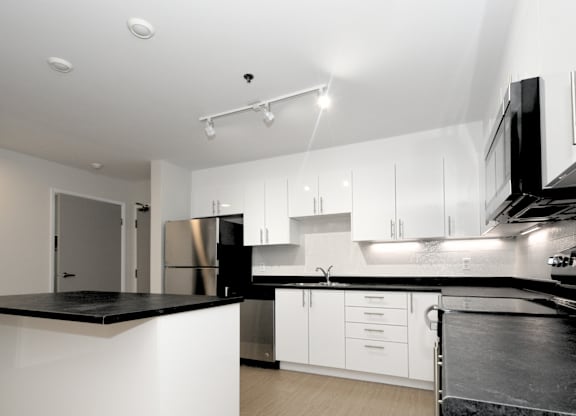 A modern kitchen with white cabinets and black countertops.