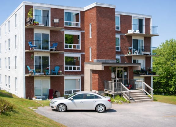A white car is parked in front of a red brick apartment building.