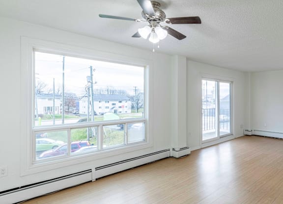 A room with a ceiling fan and large windows.