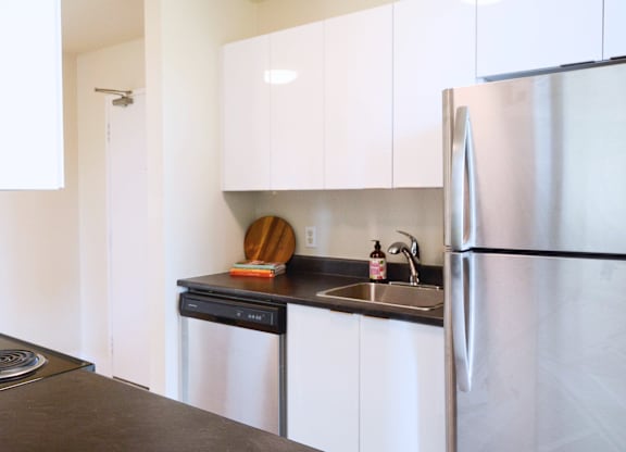A kitchen with a stainless steel refrigerator and black countertop.
