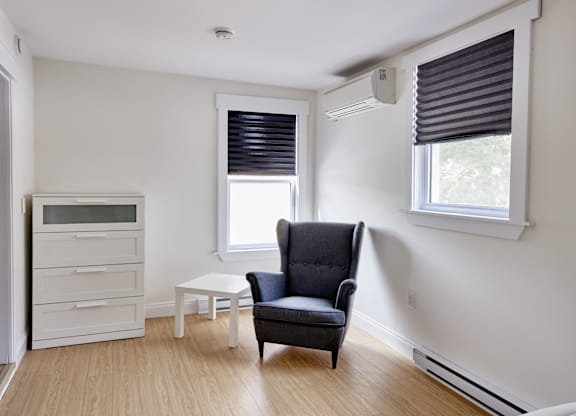 A black chair sits in a white room with a window and a white table.