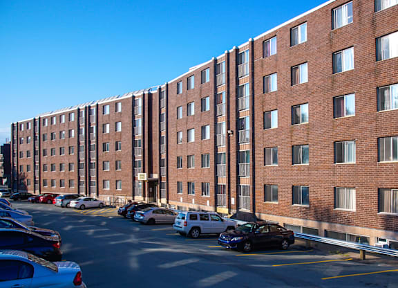 A parking lot in front of a red brick building with cars parked.
