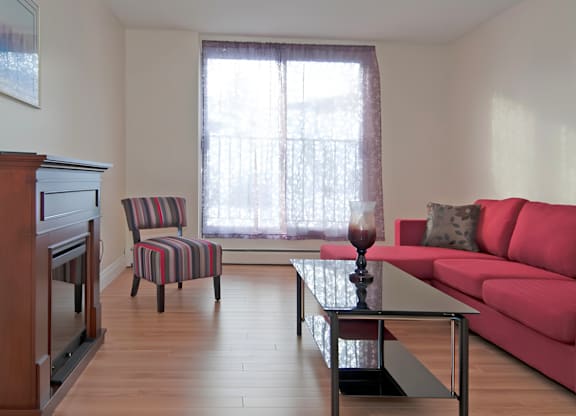 A living room with a red couch, a striped chair, and a wooden floor.
