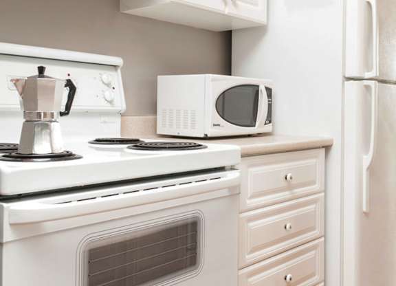 A white kitchen with a stove, microwave, and refrigerator.