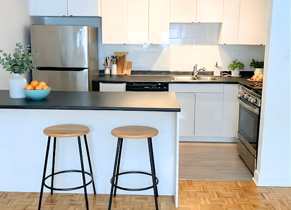 A kitchen with white cabinets and a black countertop with a refrigerator, stove, and two bar stools.