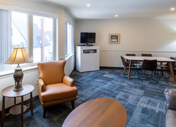 A room with a carpeted floor, a sofa, a chair, a table, a lamp, a television, and a fridge.