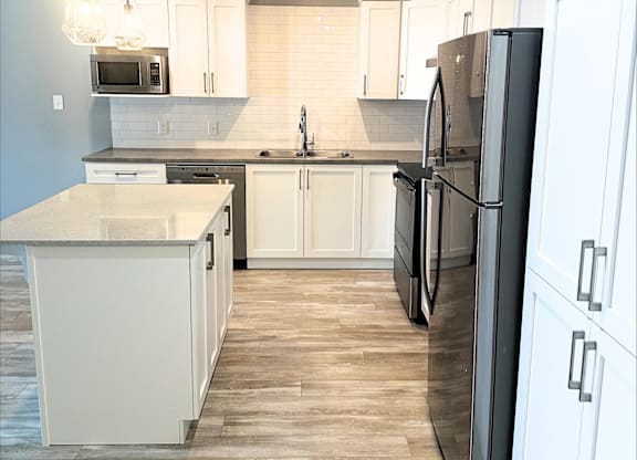 A kitchen with a black refrigerator and white cabinets.