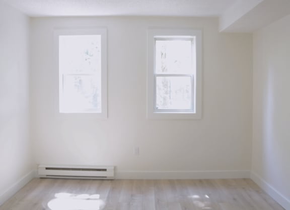 A room with two windows and a radiator on the floor.