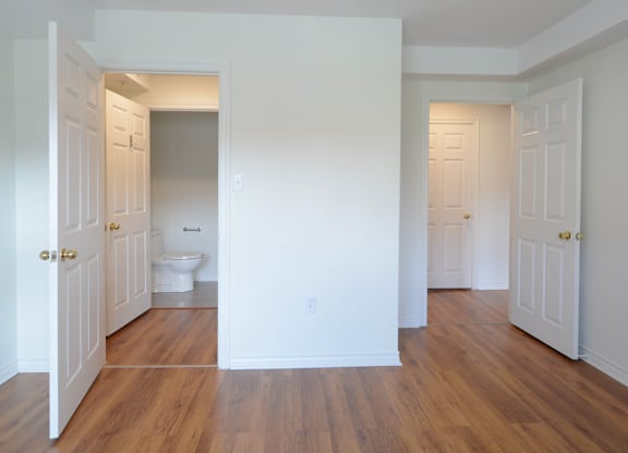 A white bathroom with wood floors and a toilet in the middle.