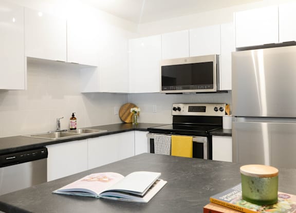 A modern kitchen with a black countertop and stainless steel appliances.