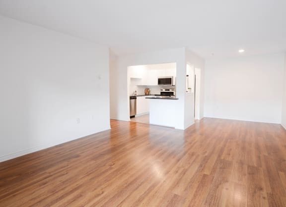 A room with wooden floors and a kitchen area in the background.