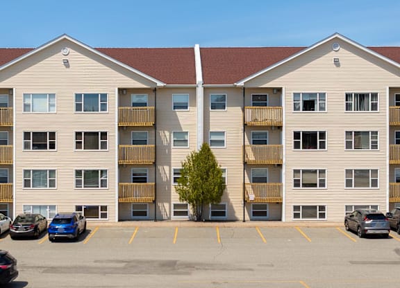 A parking lot in front of a tan apartment building with cars parked.