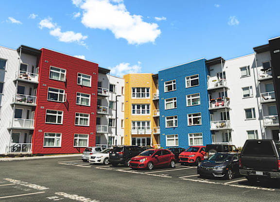 A row of colorful apartment buildings with cars parked in front.