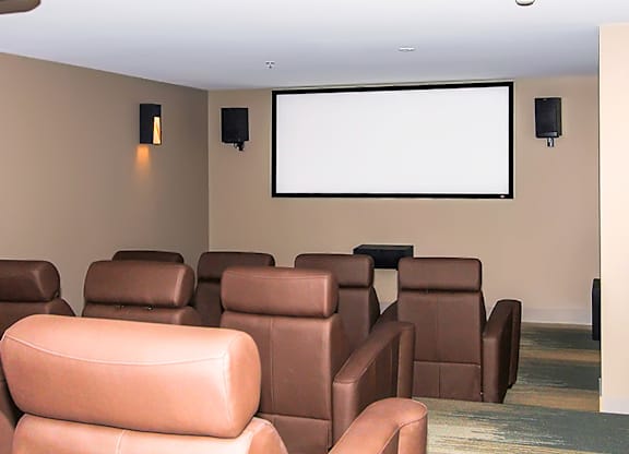 A row of brown leather chairs are arranged in front of a large screen.