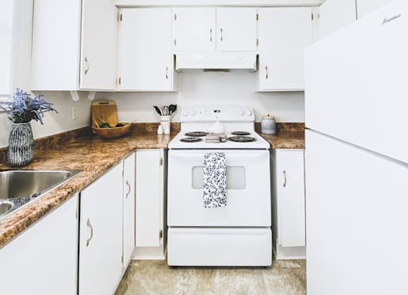 A white stove with a blue towel on it is in a kitchen with white cabinets.