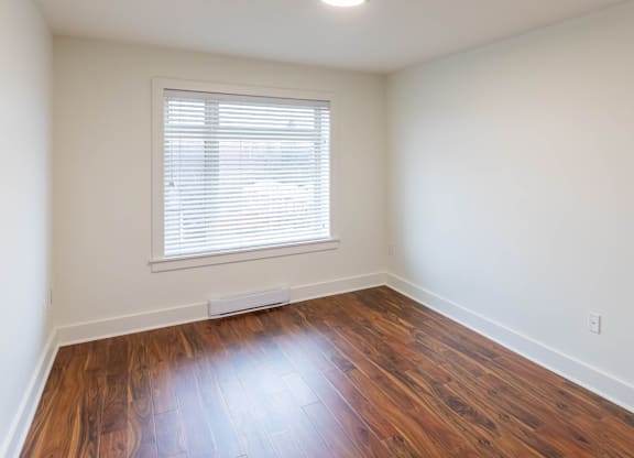A room with wooden floors and a window with blinds.