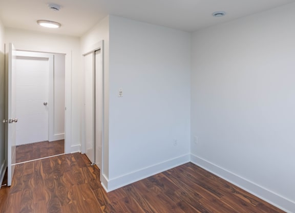 A room with white walls and wooden flooring with a door on the left.