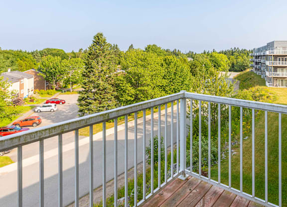 A balcony overlooks a road with cars and greenery.