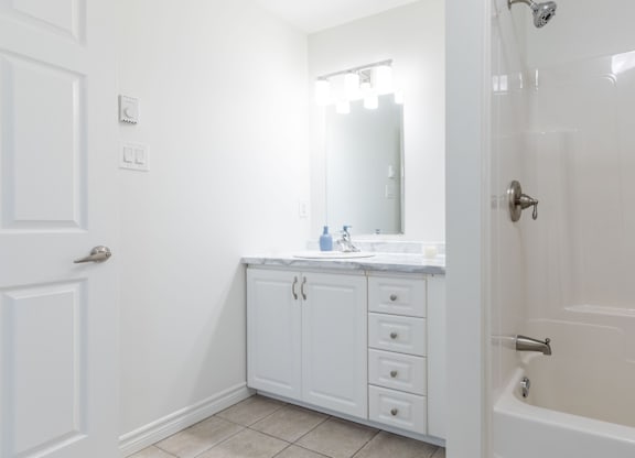 A white bathroom with a sink, mirror, and bathtub.