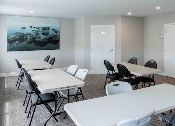 A room with white tables and chairs and a painting on the wall.