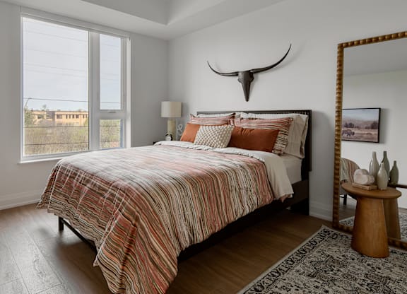 A bedroom with a bed, a mirror, and a rug.