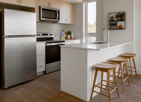 A modern kitchen with a refrigerator, stove, and bar stools.