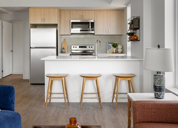 A kitchen with a white countertop and wooden bar stools.