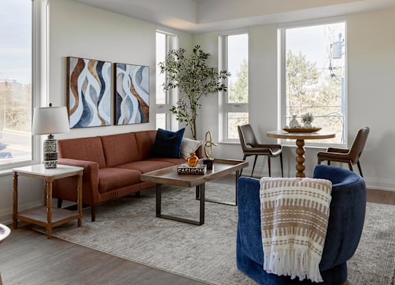 A living room with a brown couch, a blue chair, and a painting on the wall.