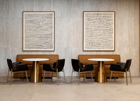 Two artworks hang on a wall above a table with chairs.
