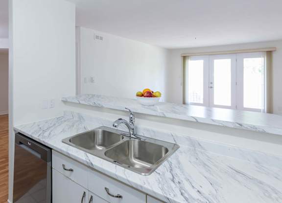 A kitchen with a marble countertop and a stainless steel sink.