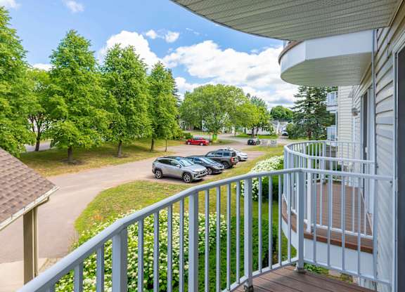 A view from a balcony overlooking a parking lot and trees.