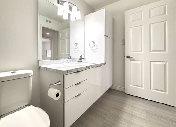 A bathroom with a toilet, sink, mirror, and a door.