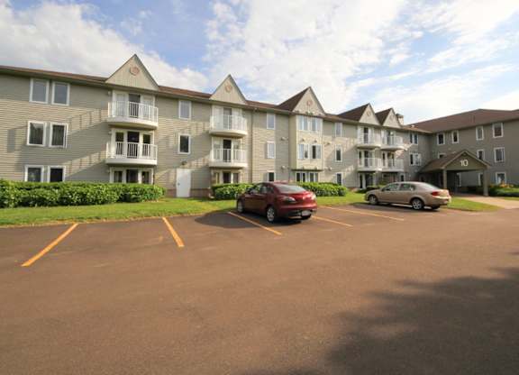 A parking lot in front of a large apartment building with two cars parked.