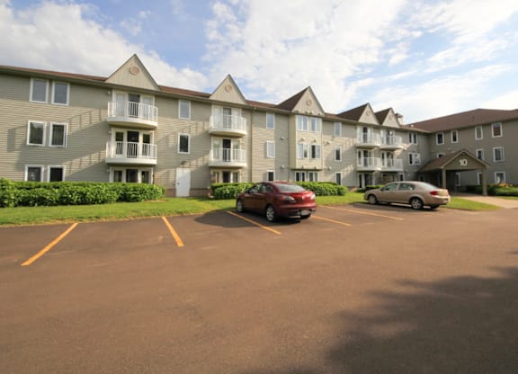A red car is parked in a parking lot in front of a building.