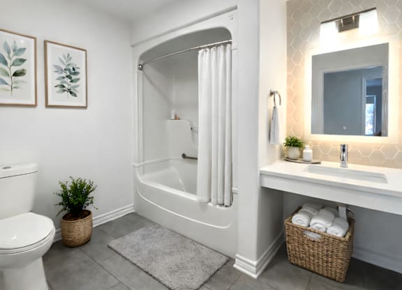 A white bathroom with a toilet, a sink, a mirror, and a potted plant.