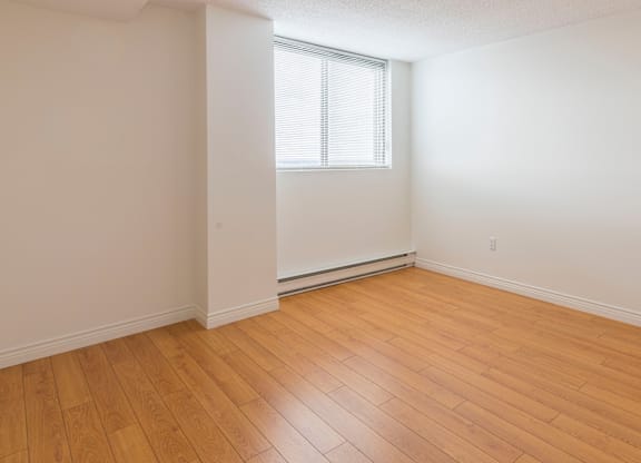 A room with wooden flooring and a window with blinds.