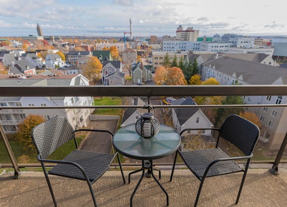 A table with two chairs is set up on a balcony overlooking a town.