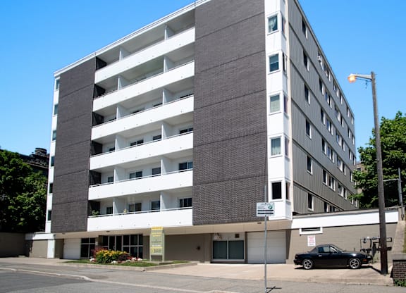 A black car is parked in front of a multi-story parking garage.