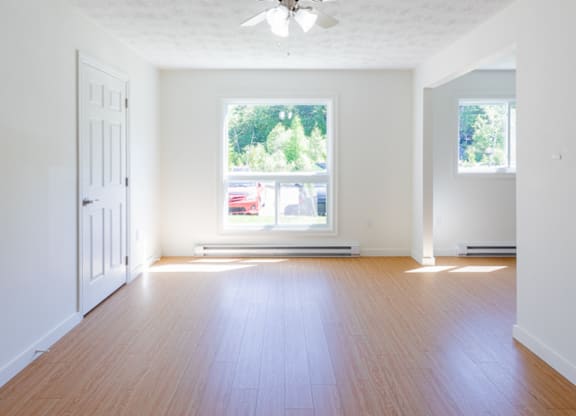 A room with a ceiling fan and a window with a view of trees and a red car outside.